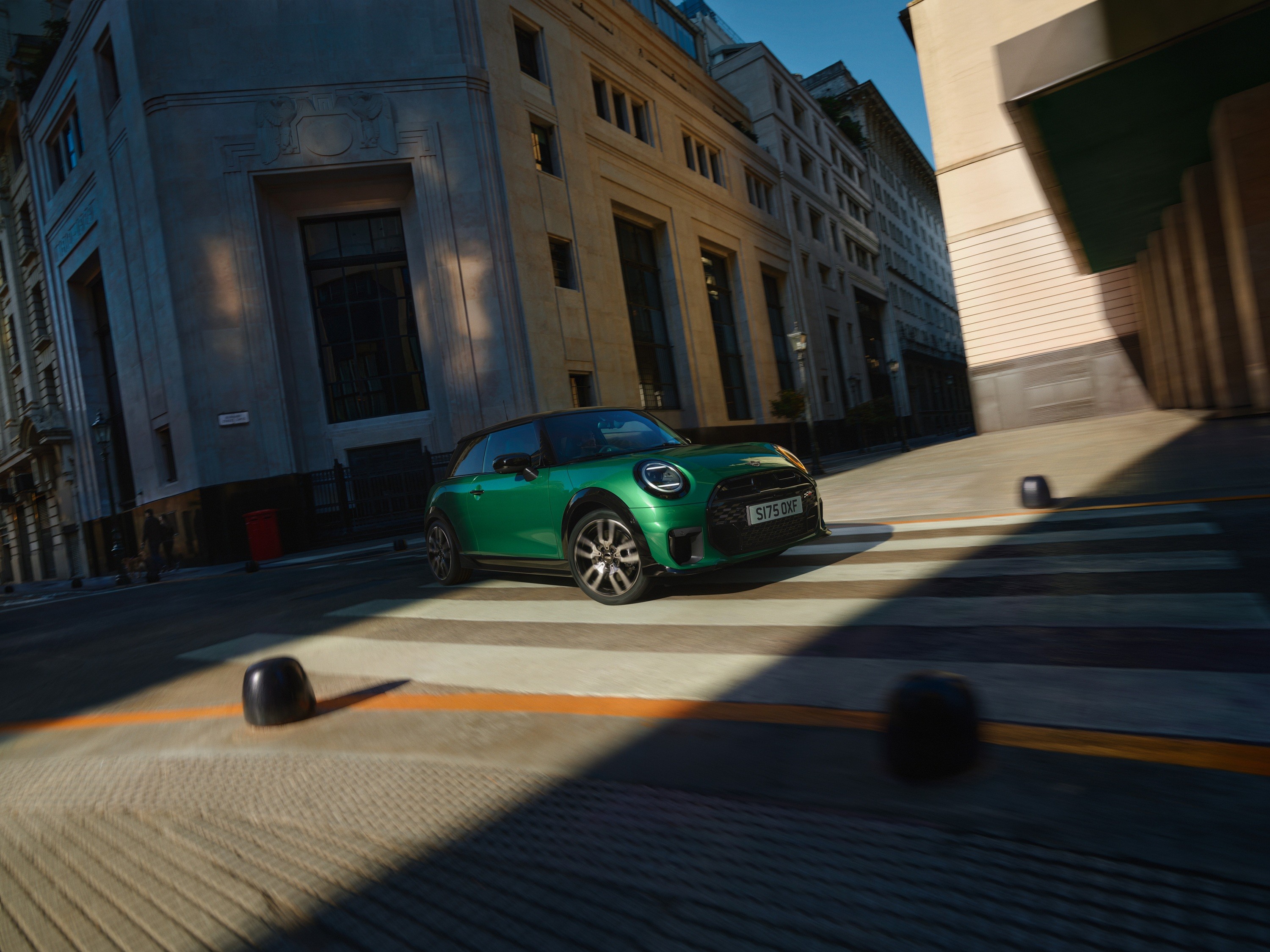 Eine Person geht über eine verschneite Fläche auf einen schwarzen MINI Cooper zu, der vor einer winterlichen Berglandschaft steht.